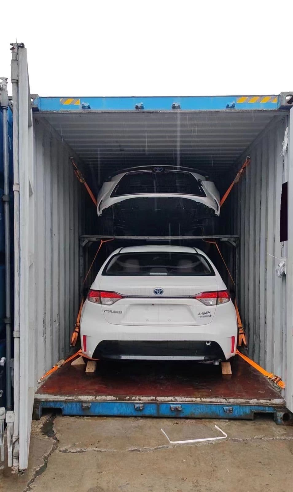 Toyota Corolla sedans secured on a two-level rack inside a shipping container